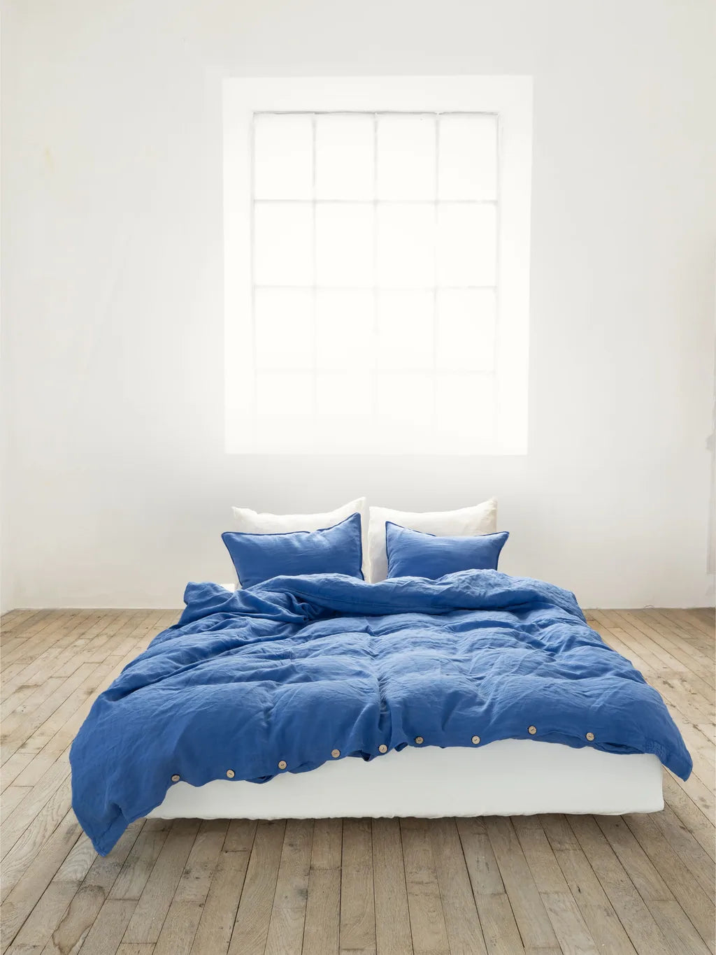 Cornflower blue Vesta linen bedding with white rear pillows and a natural buttoned duvet edge