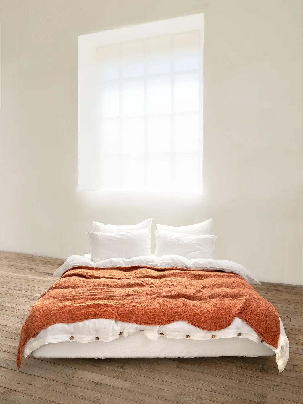 Rust blanket layered over relaxed white Vesta linen bedding